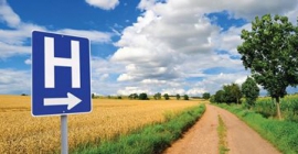 Photo of a hospital directional sign pointing down a rural road next to a field of wheat